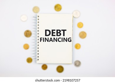 Word DEBT FINANCING On A Notepad On A White Background With Coins. The Concept Of Debt, Refinancing, Debt Relief, Credit.