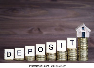 Word DEPOSIT made from wooden letter blocks and a miniature house placed on ascending coins stacks. Saving money for a mortgage deposit.