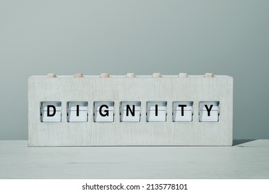 the word dignity in a rustic wooden split flap board, on a wooden surface in front of a pale gray wall - Shutterstock ID 2135778101