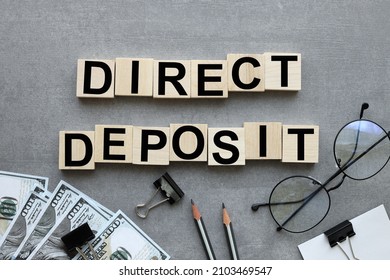 The Word Direct Deposit Text On Wood Blocks Near Money Bills On Gray Background. Business Concept