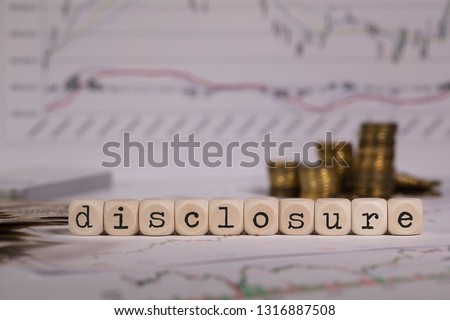 Word DISCLOSURE composed of wooden letter. Stacks of coins in the background. Closeup