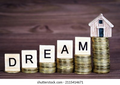 Word DREAM made from wooden letter blocks and a tiny toy house placed on ascending stacks of coins. Saving for a dream home.