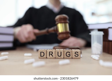 Word Drugs made with cubes and scattered pills on judge counter in courtroom. Stop illegal narcotics traffic by legal actions. Verdict for drugdealler