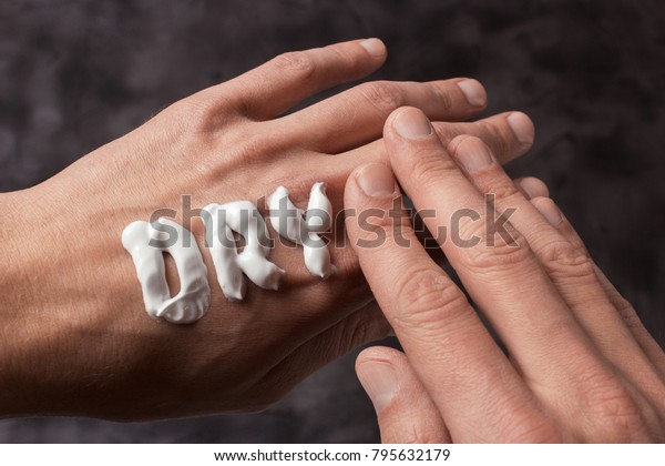 The word Dry is written in\
cream. Dry hands of a man in cream or ointment. Gray\
background