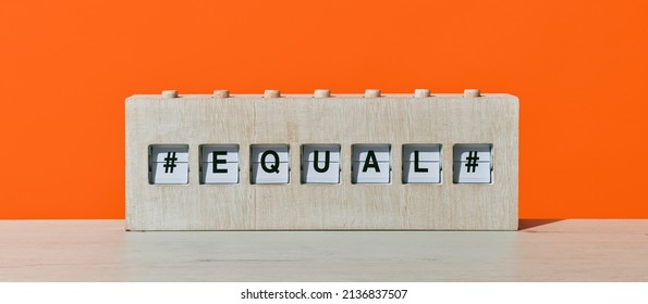 the word equal in a rustic wooden split flap board, on a wooden surface against an orange background, in a panoramic format to use as web banner or header