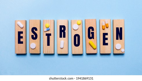 The Word ESTROGEN Is Written On Wooden Blocks On A Light Blue Table Near The Pills. Medical Concept