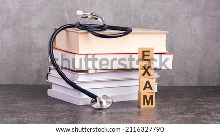 the word exam is written on wooden cubes near a stethoscope on a paper background. concept of medical education with book and stethoscope.