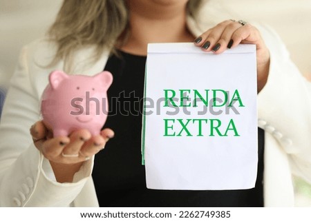 The word extra income in Brazilian Portuguese written on a notepad that a woman is holding. Brazilian economy and finance.
