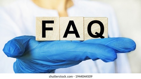 Word FAQ On Wooden Cube Blocks In The Hands In Protective Gloves Of A Doctor Woman. Blurring Doctor On Background