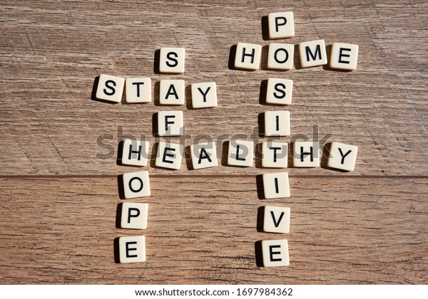 Word game with crossword\
grids showing various words - stay, home, hope, healthy, safe, and\
positive - isolated on wooden background. Stay home and be positive\
concept.