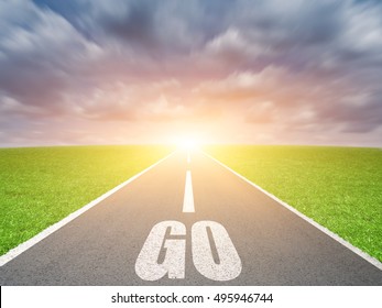The word go written on highway road in te middle of grass field against cloudy blue sky with sunrise