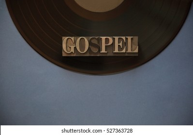 The word gospel in old metal type on a black vinyl record with a blue-gray background for text