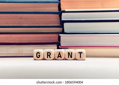 The Word Grant On Wooden Cubes Against Stacked Books Background. Education Or Research Funding Concept.