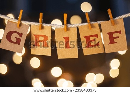 The word GRIEF printed on clothespin clipped cards in front of defocused glowing lights.