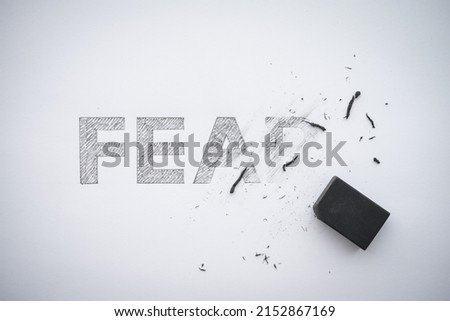 Word hand writing FEAR is deleted by black eraser on white paper background copy space. No fear or fearless concept.