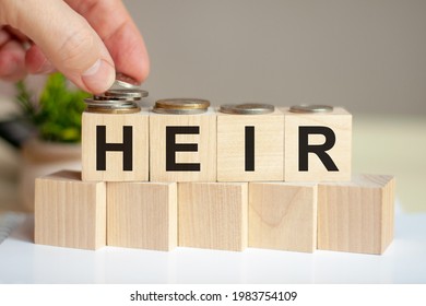The word heir written on wood cubes. A man's hand places the coins on the surface of the cube. Green potted plant on the background. Business and finance concept. - Shutterstock ID 1983754109