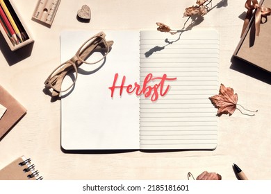 Word Herbst means Autumn in German. Wooden reading glasses, ruler, dry leaves on open notebook.