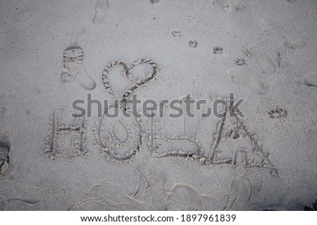 The word hi written in spanish in the sand of the beach with a heart, hola