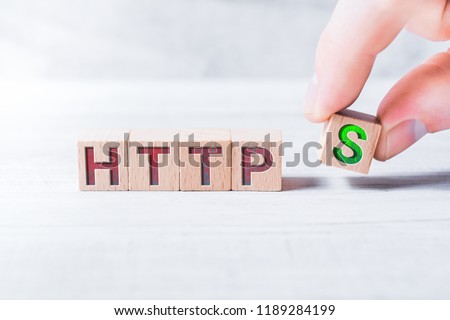 The Word HTTPS Formed By Wooden Blocks And Arranged By Male Fingers On A White Table