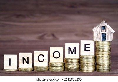 Word INCOME made from wooden letter blocks and a small toy house placed on ascending coins stacks. Increasing income for a mortgage deposit.