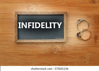 Word Infidelity written on mini blackboard and two rings on the left side of the board. Concept of adultery,infidelity,marriage and relationship problem.