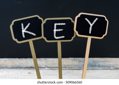 Word KEY written with chalk on wooden mini blackboard labels, defocused chalkboard and wood table in background