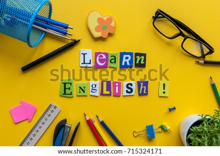 Word LEARN ENGLISH made with carved letters onyellow desk with office or school supplies, stationery. Concept of English language courses