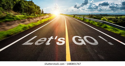 The word let's go written on highway road in the middle of empty asphalt road at  beautiful blue sky.