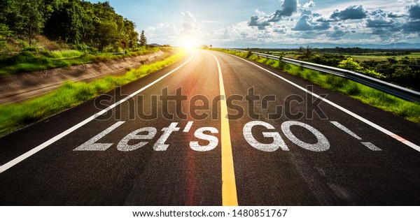 The word let\'s go\
written on highway road in the middle of empty asphalt road at \
beautiful blue sky.
