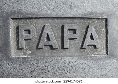 The word, letters, and text of Papa carved into the natural stone tombstone.