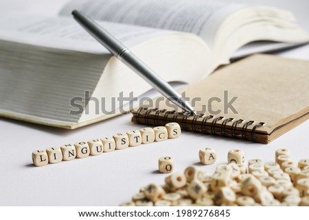 The word linguistics next to notebook, pen and open book. A concept for college liberal arts studies and contemporary language history studies. White background. Macro. Selective focusing. Close-up