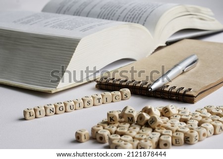 Word linguistics next to notebook, pen, open book and many letters. Concept of the study of the humanities and modern studies of the history of language. White background. Selective focus. Macro