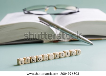 The word linguistics is written next to open book, pen and. Concept for the study of linguistics at school, college and university. Pastel background. Selective focusing. Close-up