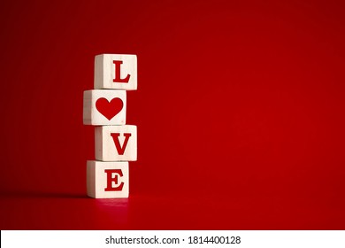 The word love with a heart shape on wooden cubes against red background. Love, romance, relationship or valentines day concept.