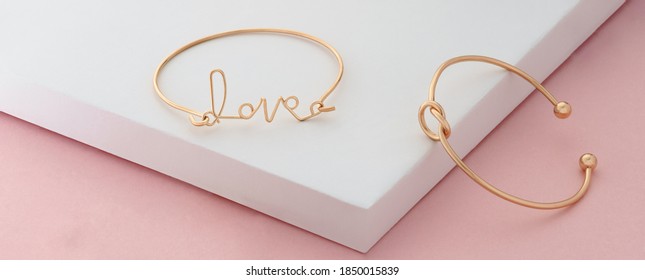 Word love and knot shape golden bracelets on pink and white background