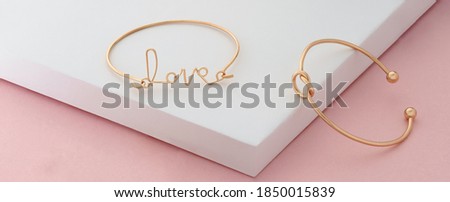 Word love and knot shape golden bracelets on pink and white background