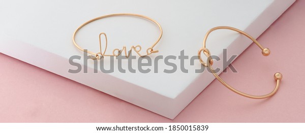 Word love and knot shape golden bracelets on\
pink and white background