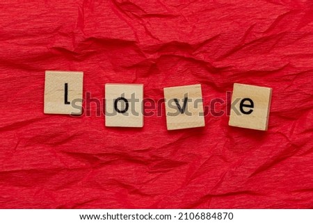 The word Love, laid out in wooden cubes on crumpled red paper. A declaration of love for your girlfriend, boyfriend, for a romantic Valentine's Day greeting card