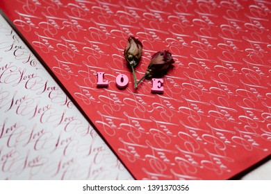 Word LOVE made up from wooden pink letters and two dried flowers insted of letter V. Calligraphic writing with ink on red and white paper 