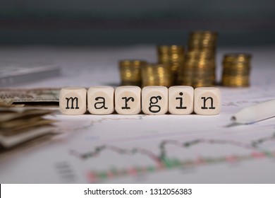 Wort MARGIN besteht aus Holzbuchstaben. Stapel von Münzen im Hintergrund. Nahaufnahme