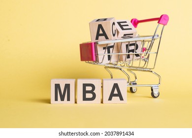 The Word MBA - Master Of Business Administration, On Wooden Cubes, On A Yellow Background With A Shopping Trolley.