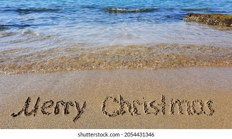 Word Merry Christmas written on the sand near the sea.