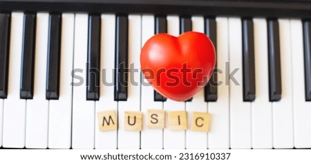 Word music made by wooden cubes on a s ynthesizer keys black and white background with a red heart. Piano octave close up top view. Keyboard musical instrument. love music concept