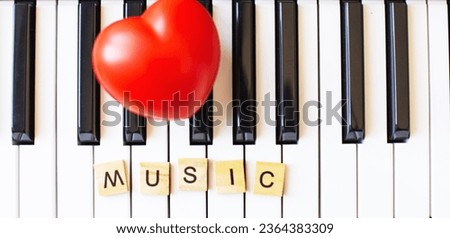 Word music made by wooden cubes on a s ynthesizer keys black and white background with a red heart. Piano octave close up top view. Keyboard musical instrument. love music concept