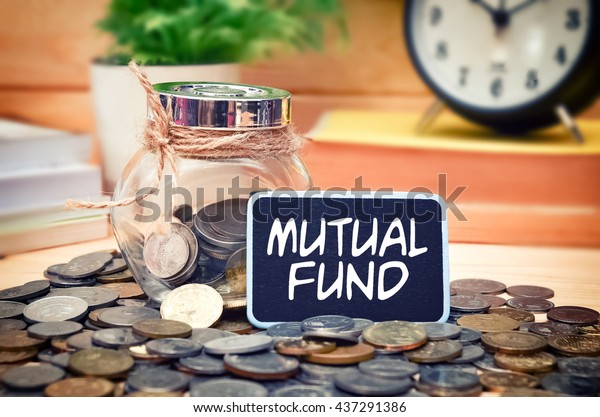 Word Mutual Fund on mini chalkboard and coin in\
the jar with blurred background of books, green plant and clock.\
Financial Concept.