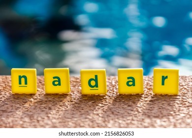 Word Nadar Which Means To Swim In Spanish Made Of Scrabble Type Letters By The Edge Of Swimming Pool. 