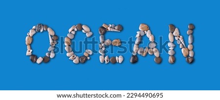 The word "OCEAN" lined with seashells and stones of different shapes and colors on a harmonious blue background. The concept of ecology and ocean rescue, marine alphabet.