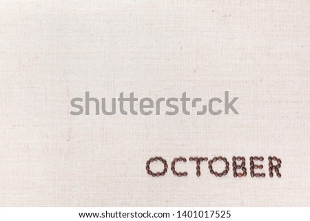 The word October written with coffee beans on creamy linea canvas, shot from above, aligned at the bottom right.