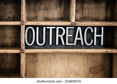 The word "OUTREACH" written in vintage metal letterpress type in a wooden drawer with dividers.