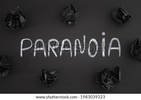 The word Paranoia on a black background with black crumpled paper balls around it. Close up.